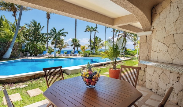A poolside area with a table, chairs, and a fruit bowl. - Beachfront Condo with Pool Access (Akumal Sur)