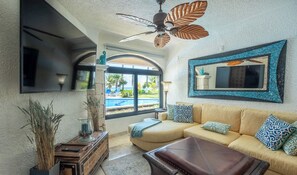 Ein Wohnzimmer mit einer Couch, einem Couchtisch, einem Kamin, einem Deckenventilator und Blick auf einen Pool.