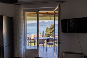 Ein Zimmer mit einer Schiebeglastür, die auf einen Balkon mit Blick auf Meer und Berge führt.