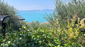 A view of a coastal landscape with a clear sky, a body of water, and some vegetation in the foreground. - Jordan House (Torri del Benaco)