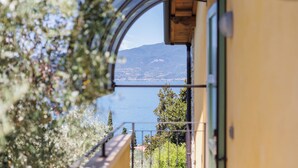 A view through a window of a building with a balcony overlooking a body of water and a mountain. - Jordan House (Torri del Benaco)