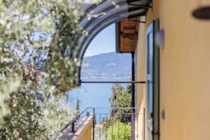 Blick durch ein Fenster auf ein Gebäude mit Balkon, das auf ein Gewässer und einen Berg blickt.