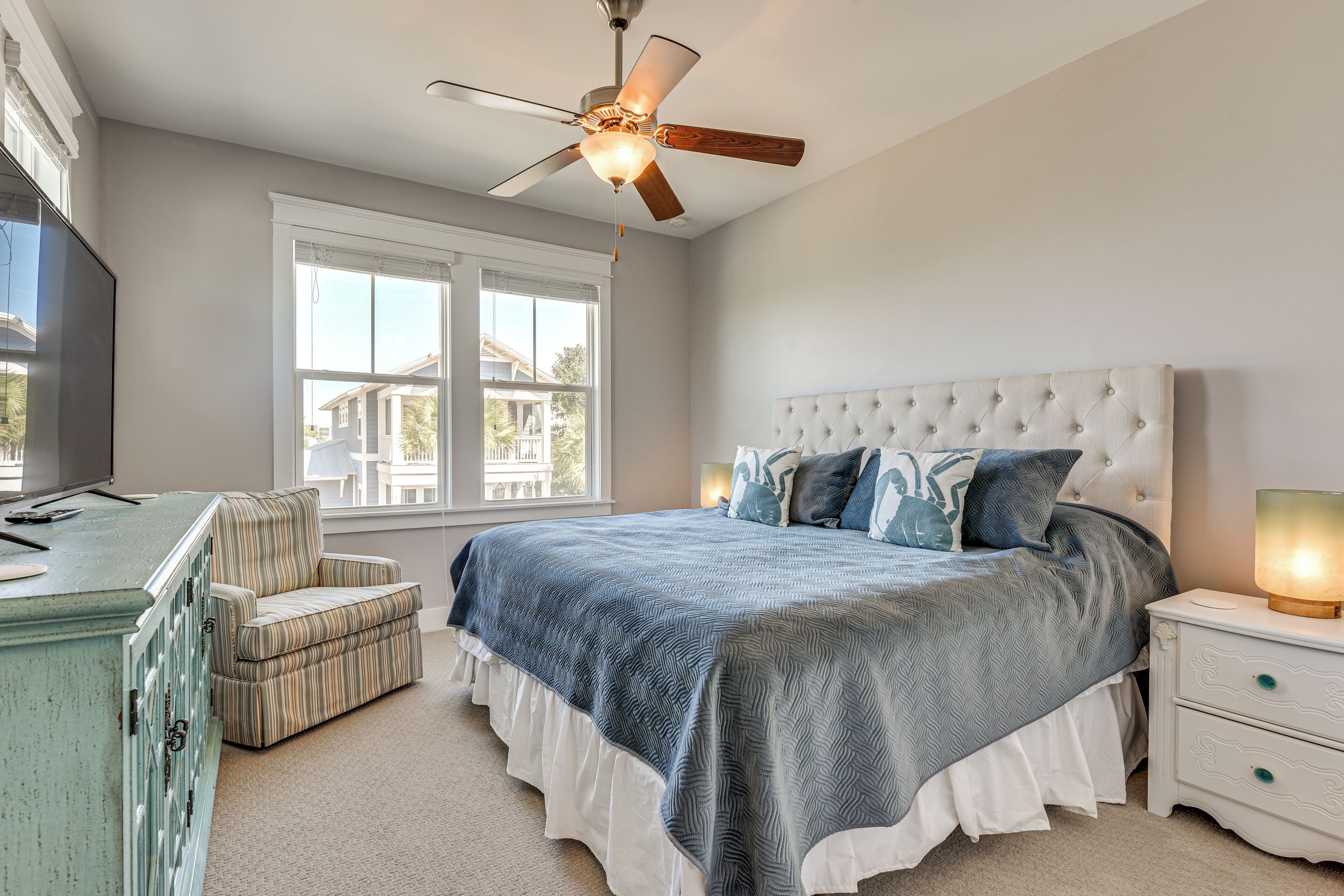 A bedroom with a bed, a ceiling fan, a window, a dresser, and a chair.