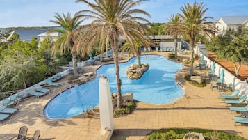 Un espace piscine avec des chaises longues, des palmiers et une vue sur la mer.