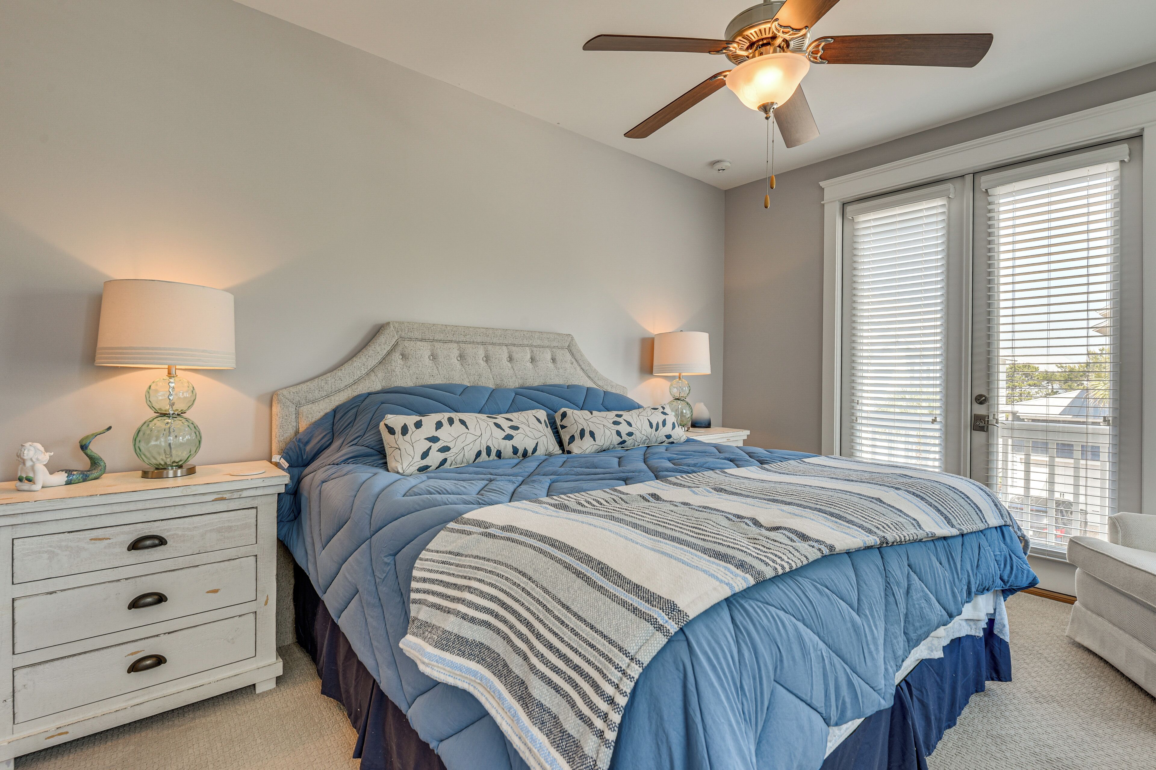 A bedroom with a bed, nightstands, lamps, a ceiling fan, and a view through the window.
