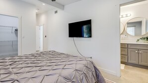 Ein Schlafzimmer mit Bett, Deckenventilator, Wand-TV und eigenem Badezimmer mit Spiegel und Waschbecken.