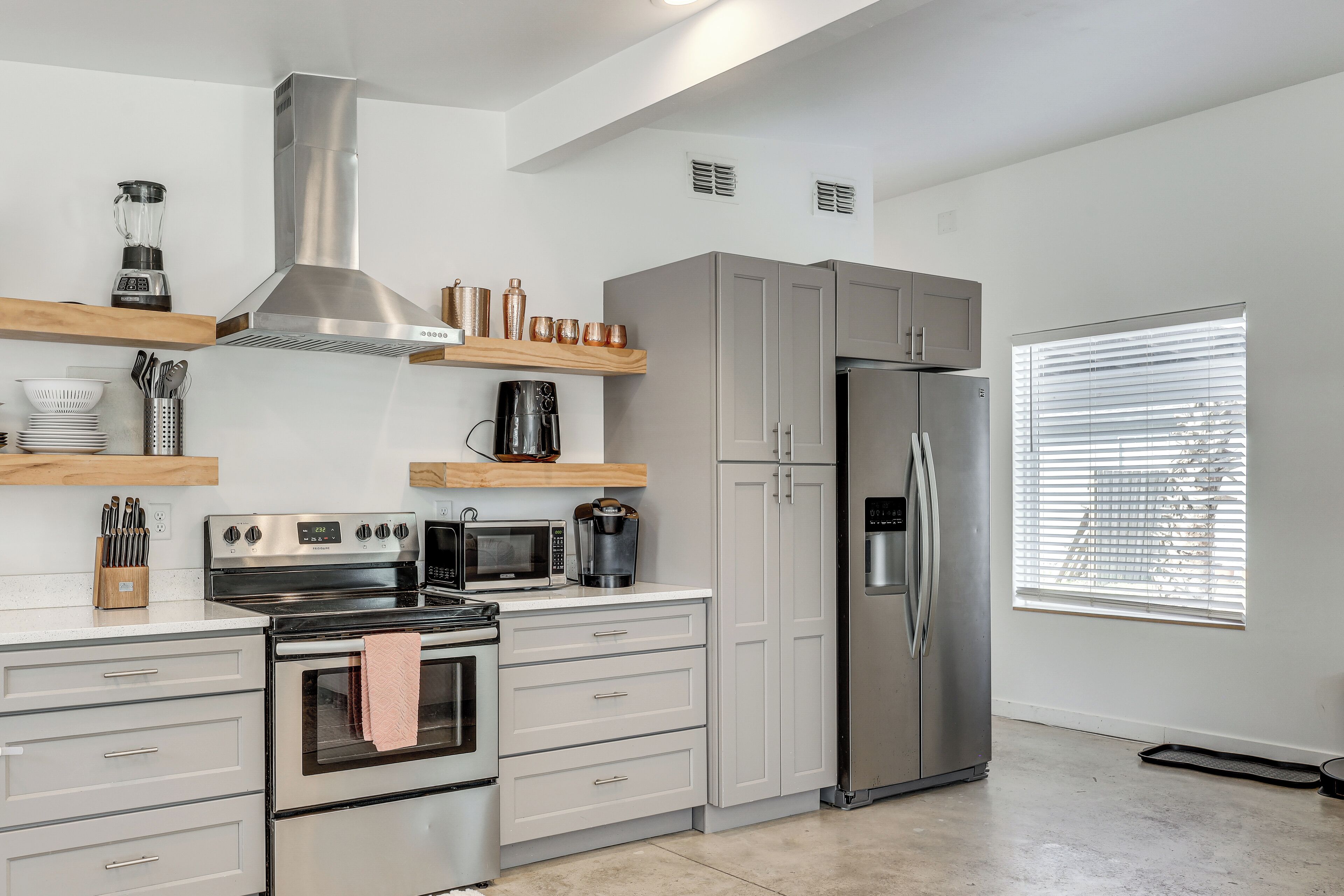 A modern kitchen with stainless steel appliances, wooden shelves, and a large window.