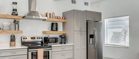 A modern kitchen with stainless steel appliances, wooden shelves, and a large window.