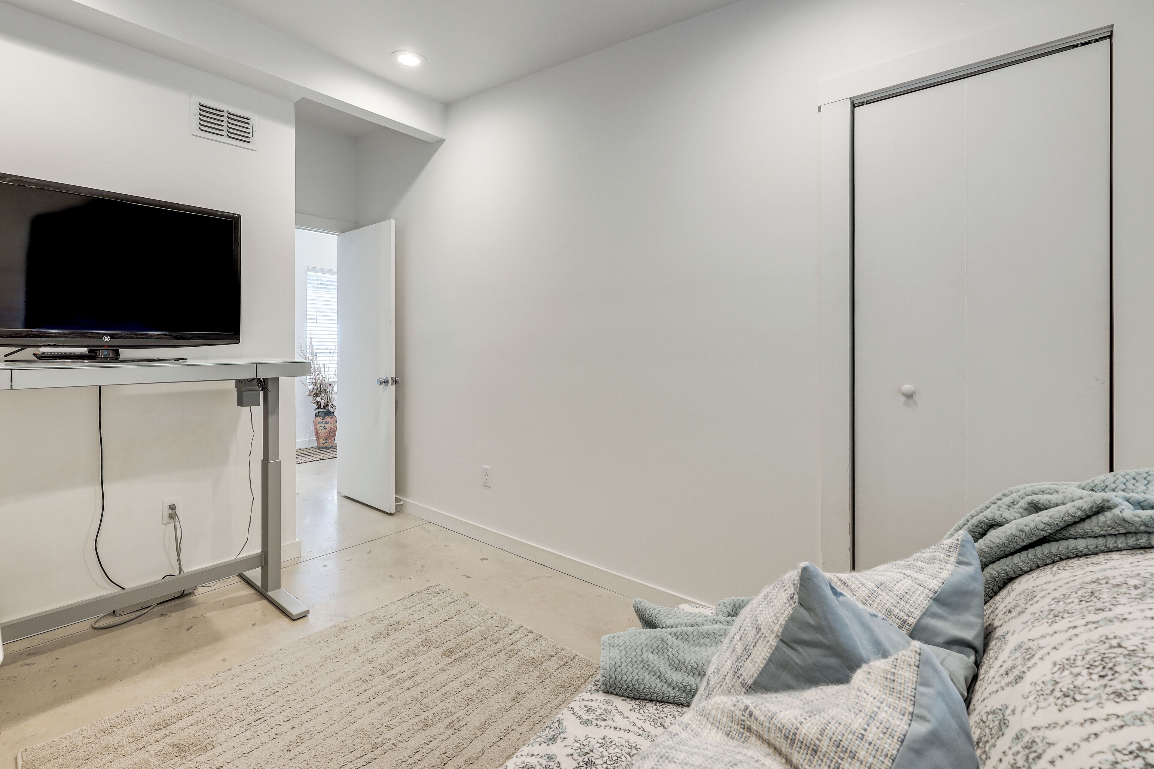 A bedroom with a bed, a TV on a stand, a door, and a window.