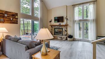 A spacious living room with a fireplace, large windows, a sofa, and a television.