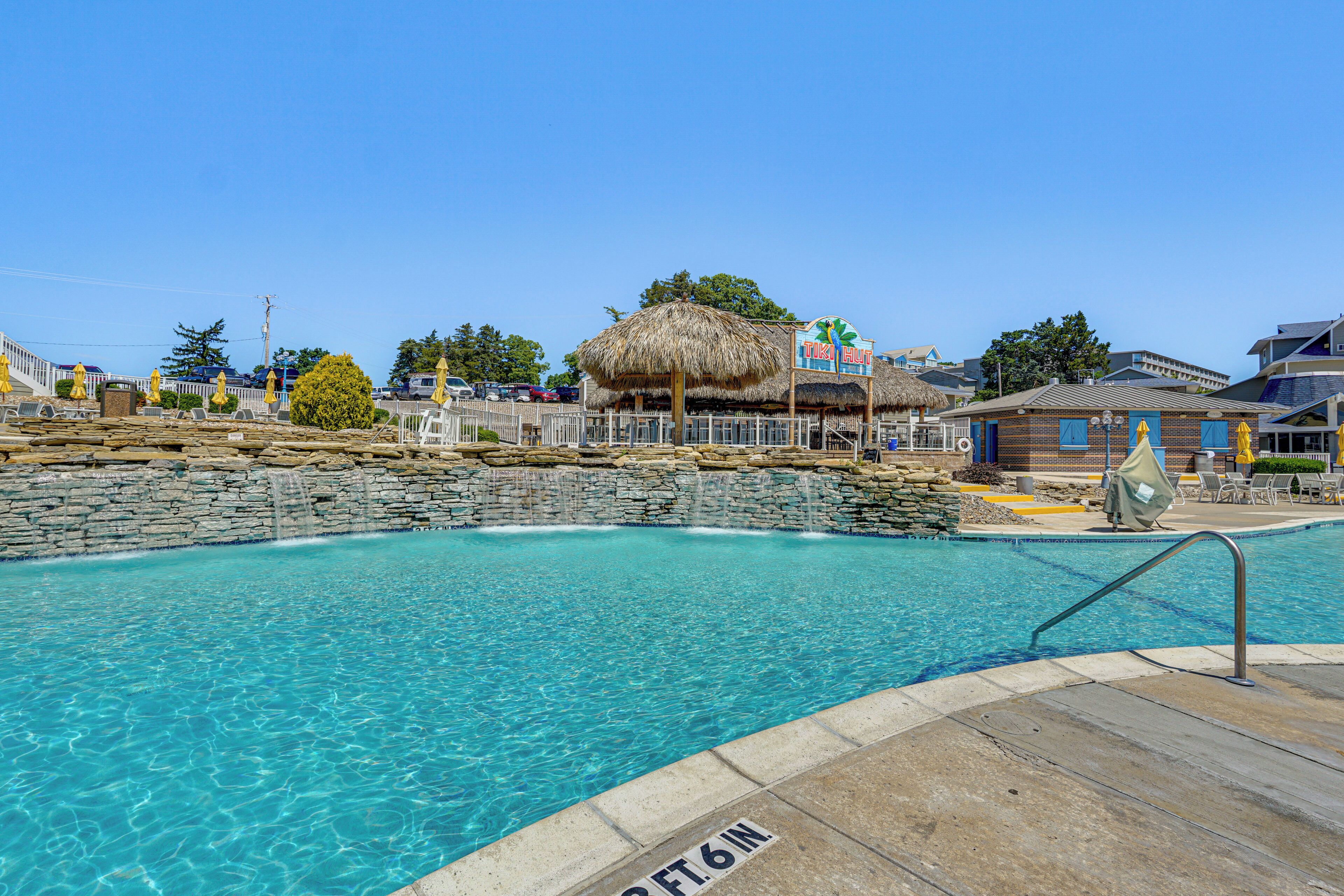 Une piscine dotée d’une structure de toit en chaume, d’un mur en pierre et d’une enseigne indiquant : « The But ».