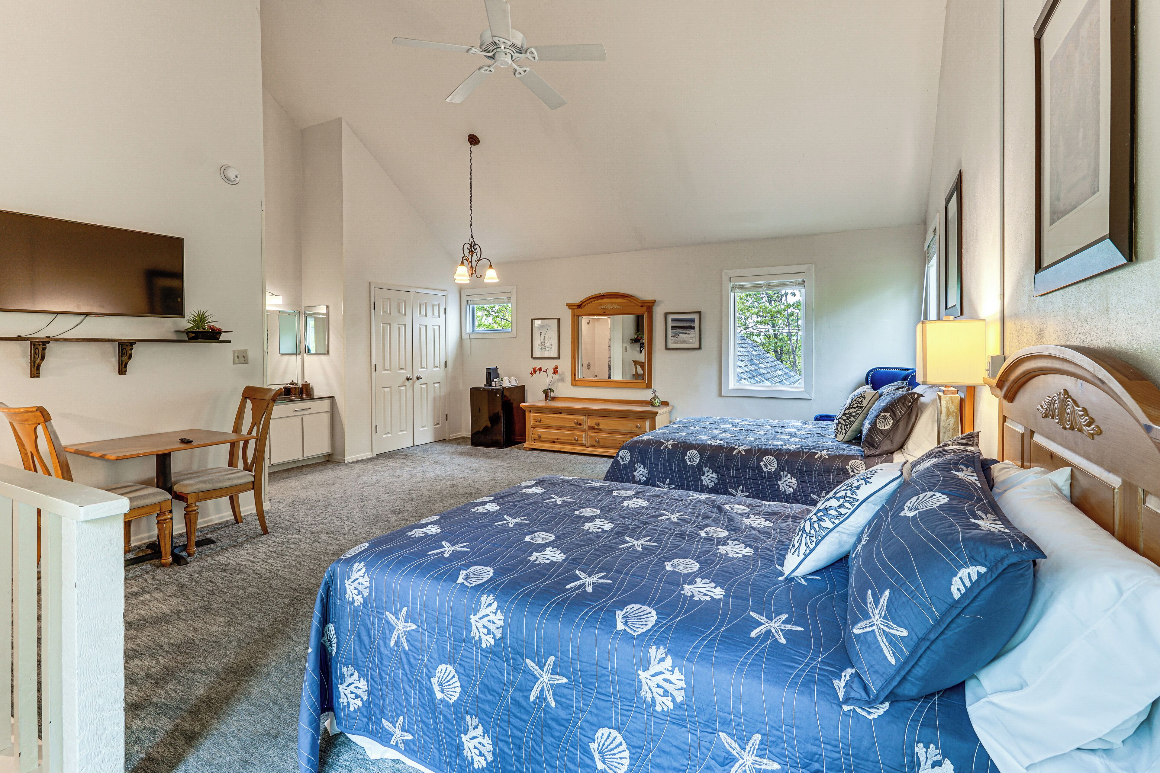 A bedroom with two beds, a desk, a chair, a dresser, a mirror, and a ceiling fan.
