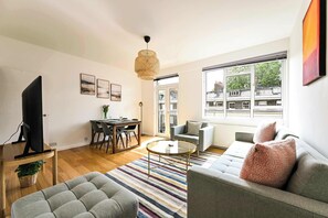 A modern living room with a sofa, armchair, dining table, and a TV. - British Museum Apartment (Greater London)