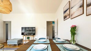 Un coin repas avec une table en bois dressée pour quatre personnes, un téléviseur et un vase rempli de fleurs.