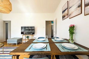 Een eethoek met een houten tafel gedekt voor vier personen, een televisie en een vaas met bloemen.