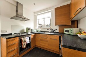 A modern kitchen with wooden cabinets, a gas stove, a built-in oven, and a window providing natural light. - British Museum Apartment (Greater London)