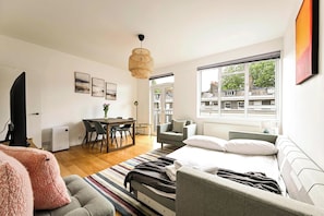 Een moderne slaapkamer met een bed, een bank, een eethoek en uitzicht op gebouwen door grote ramen.