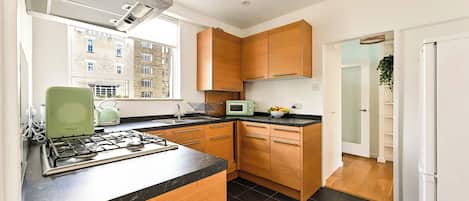 Una cocina moderna con estufa a gas, armarios de madera, microondas y vistas a la ciudad a través de un ventanal.