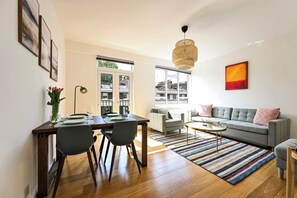 A modern living room with a sofa, a dining table with chairs, a striped rug, and a hanging light fixture. - British Museum Apartment (Greater London)
