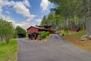 A red cabin with a stone foundation, a porch, and a green roof, surrounded by a forested area. - Butler Cabin w/ 2 Decks: Near Watauga Lake! (Mountain City)