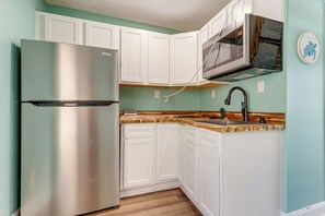 Eine Küche mit weißen Schränken, einem Edelstahl-Kühlschrank, einer Mikrowelle und einer Holz Arbeitsplatte.