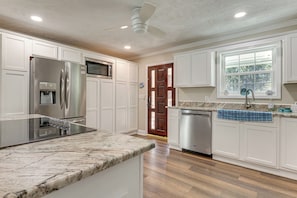 A kitchen with white cabinetry, a stainless steel refrigerator, a dishwasher, and a marble countertop. - Beaches, Fishing & More! Home on Dauphin Island (Dauphin Island)