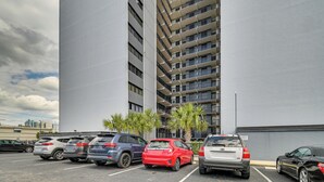 Een parkeerplaats met diverse auto's, een hoog gebouw met meerdere balkons en enkele palmbomen.