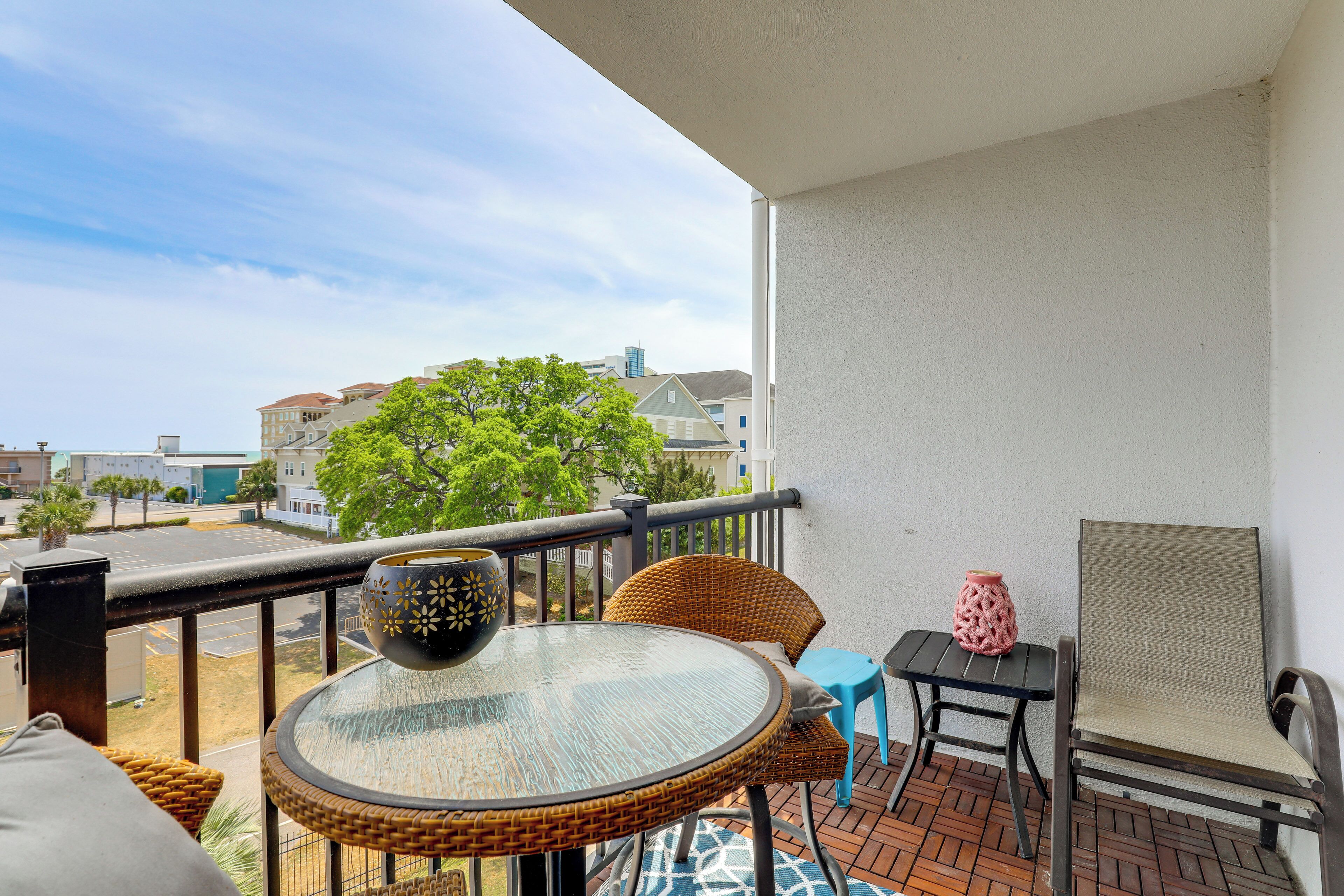 En balkon med et rundt bord, fletstole, en blå stol, en pink vase og en fletkurv.