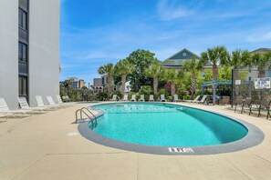 A swimming pool with lounge chairs, a lifeguard sign, and a building in the background. - Walk to Family Kingdom! Condo w/ Pool + Balcony (Myrtle Beach)