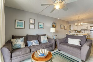 A living room with two grey sofas, a wooden coffee table with a starfish, a ceiling fan, and a kitchen in the background. - Walk to Family Kingdom! Condo w/ Pool + Balcony (Myrtle Beach)