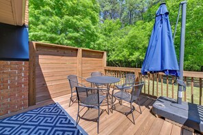A deck with a grill, a table with chairs, and a blue umbrella.