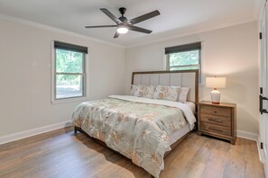 A bedroom with a bed, a nightstand, a lamp, a ceiling fan, and two windows. - 4 Mi to Charlotte Speedway! Extended Wooded Escape (Harrisburg)