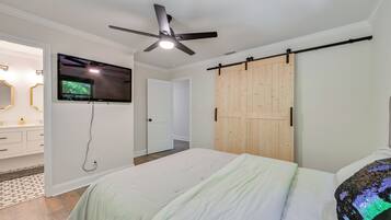 A bedroom with a bed, a ceiling fan, a TV mounted on the wall, and a wooden sliding door.