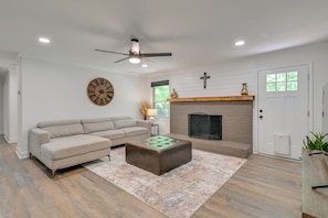 Un salon comprenant un canapé, un pouf, une cheminée, un ventilateur de plafond et une horloge murale.