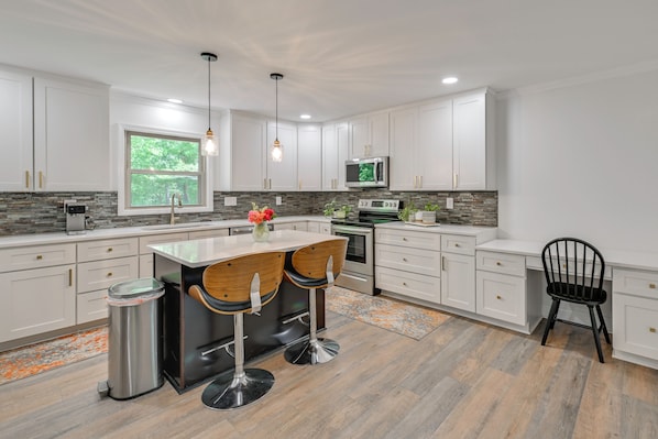 A modern kitchen with white cabinets, a stainless steel sink, a microwave, and a large window.