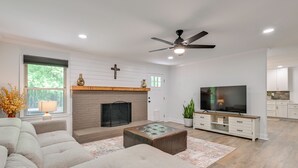A modern living room with a fireplace, sofa, coffee table, TV, and a ceiling fan. - 4 Mi to Charlotte Speedway! 3BD Home w/ Deck (Harrisburg)