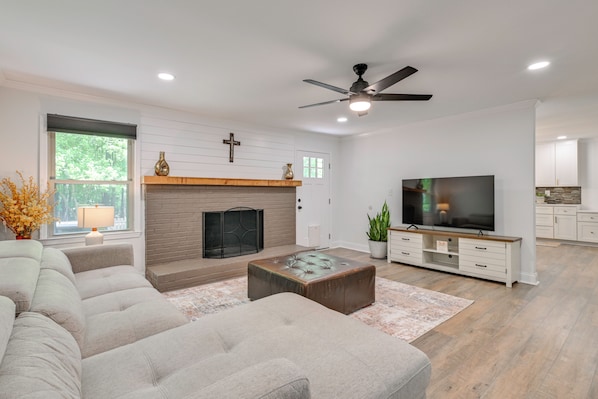 A modern living room with a fireplace, sofa, coffee table, TV, and a ceiling fan.