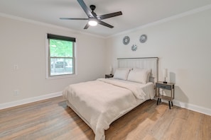 A bedroom with a bed, a nightstand, a ceiling fan, a window, and wall decorations.