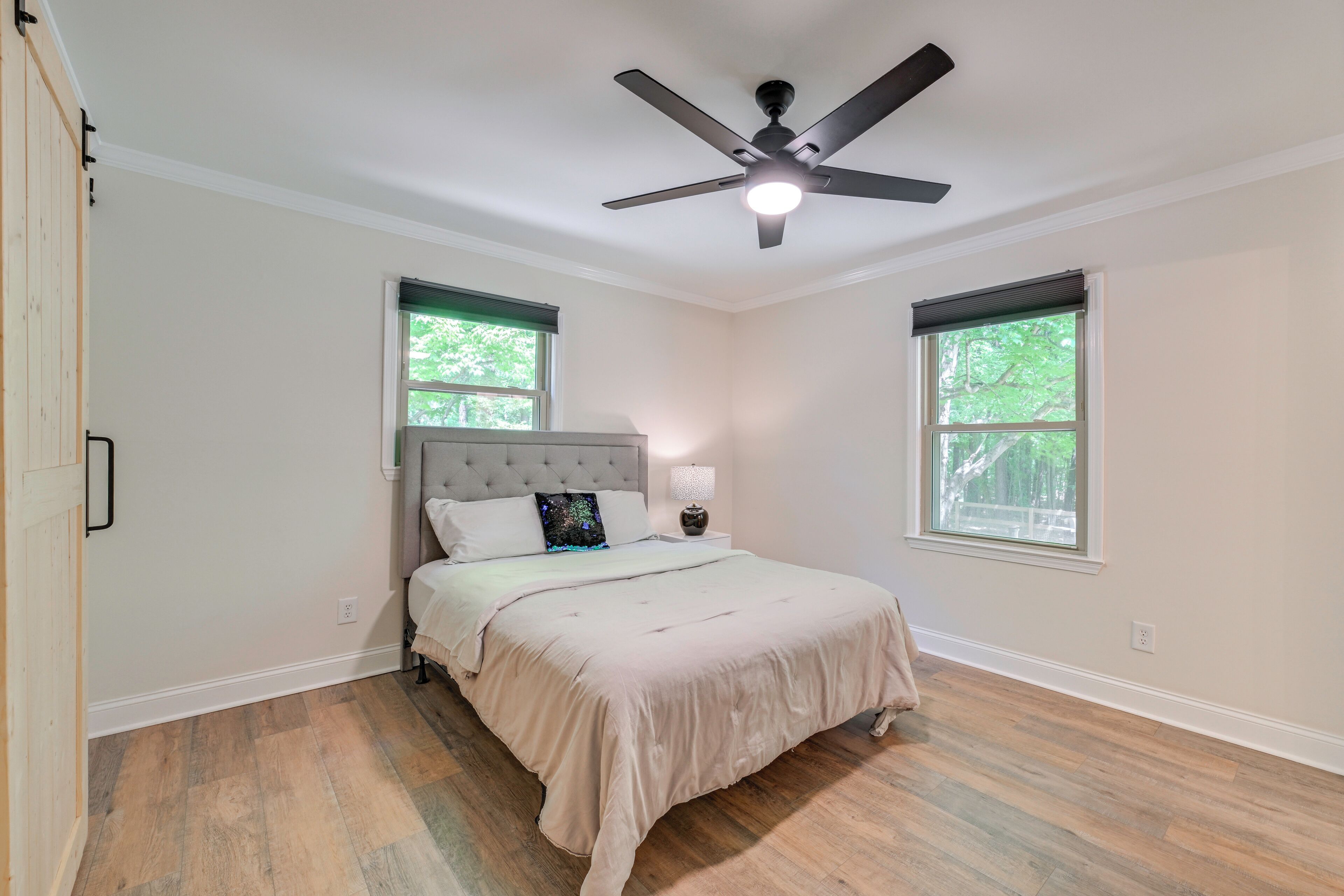A bedroom with a bed, a ceiling fan, two windows, and a nightstand with a lamp.