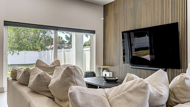 A modern living room with a sofa, television, and a dining table. - Private Yard & Covered Patio: Modern Tampa Getaway (Tampa)