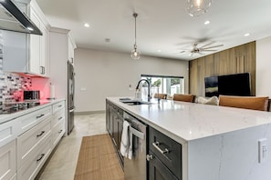 A modern kitchen with white cabinetry, a marble island, a built-in oven, and a ceiling fan.