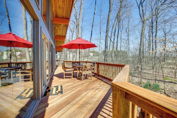 A wooden deck with outdoor seating and red umbrellas, overlooking a forested area.