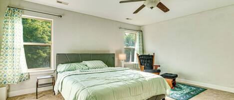 A bedroom with a bed, a ceiling fan, a window with curtains, a nightstand, a chair, and a small table.