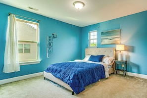 A bedroom with a bed, a nightstand, a lamp, a window with a curtain, and a wall with a painting and a 'HOME' sign.