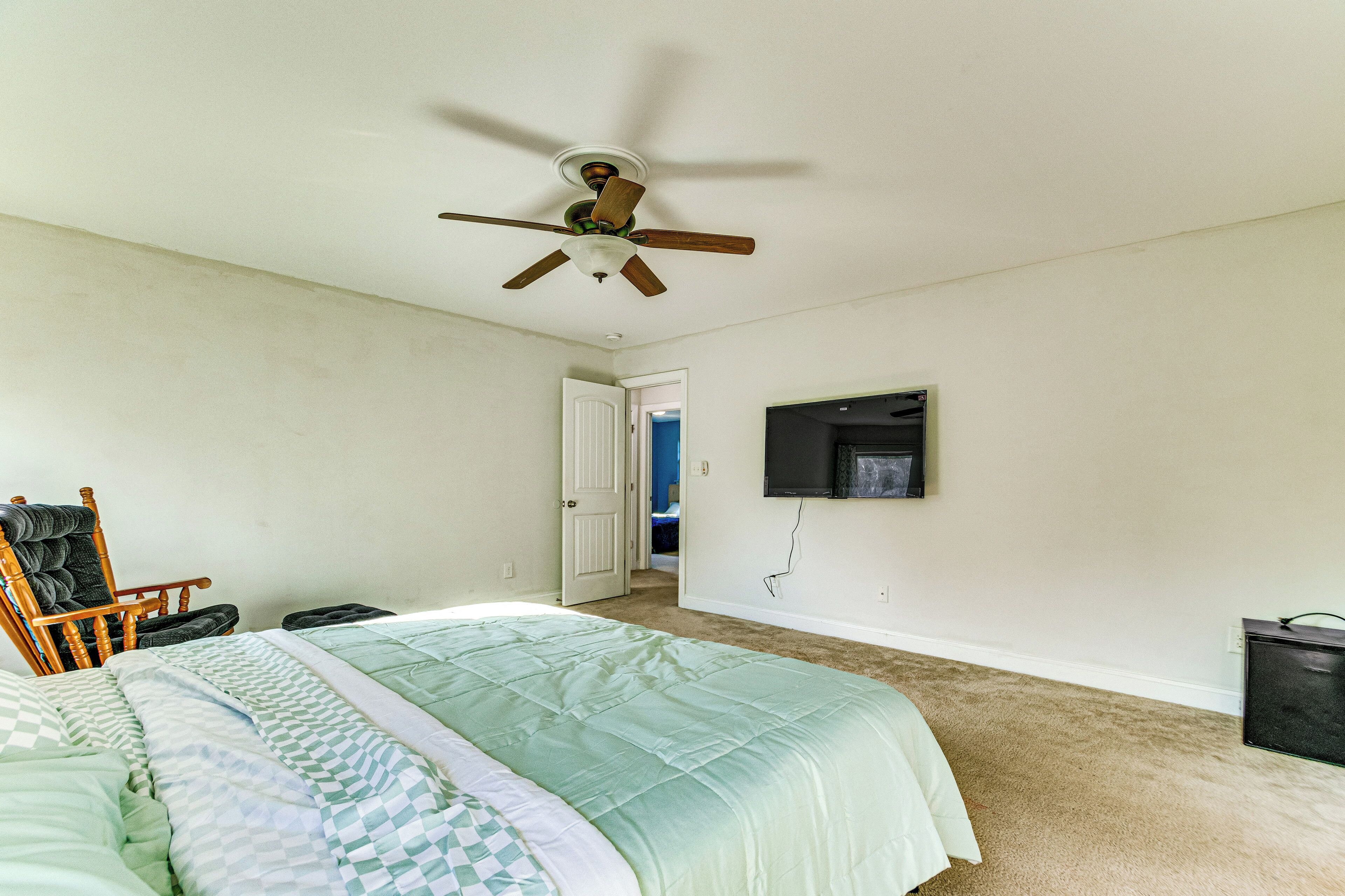 Una camera da letto con un letto, una ventola a soffitto, una sedia, una televisione e una porta che dà su un'altra stanza.