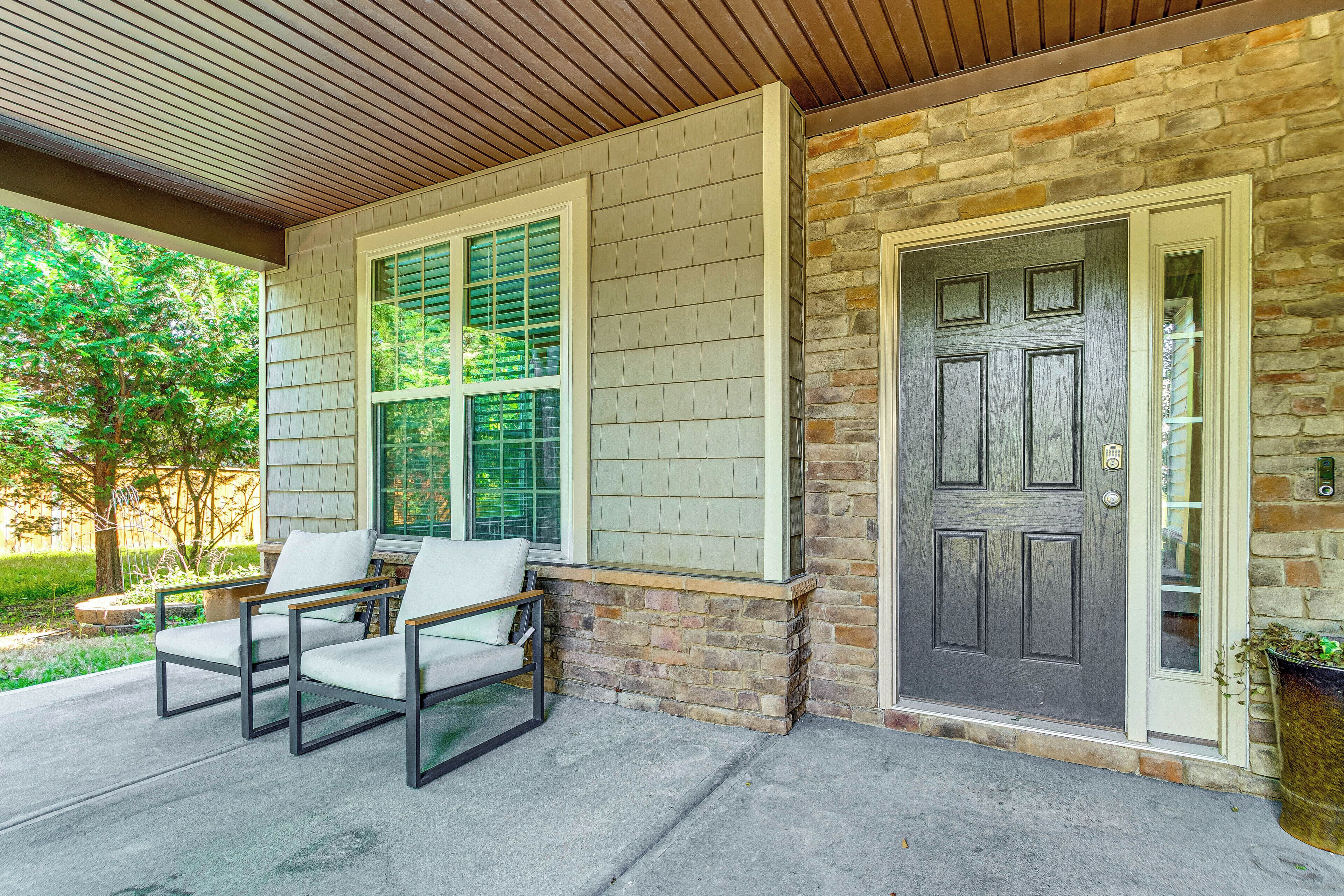 A house exterior with a covered porch, two chairs, a door, and a window with shutters.