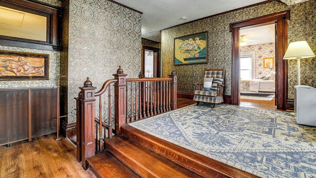 Una habitación con alfombra estampada, una escalera de madera, una silla, una cama y un cuadro en la pared.