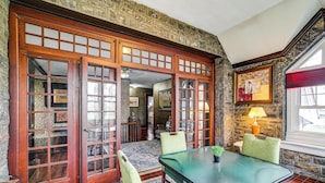 Una habitación con una puerta de madera grande, una mesa con sillas, una lámpara y una pared de piedra.