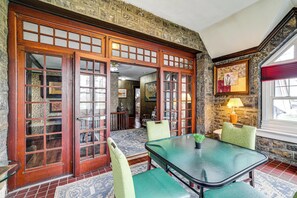 Um quarto com uma grande porta de madeira, uma mesa com cadeiras, um abajur e uma parede de pedra.
