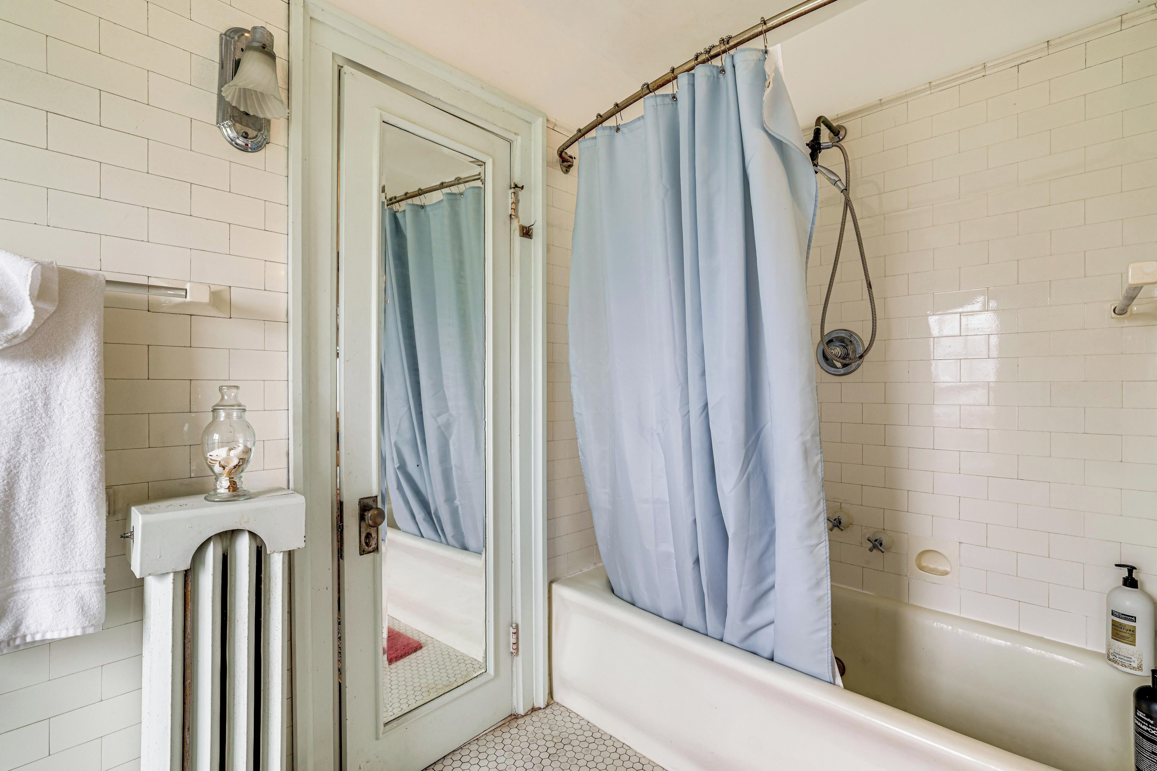 Une salle de bain avec une baignoire, un rideau de douche, un porte-serviettes et un miroir.
